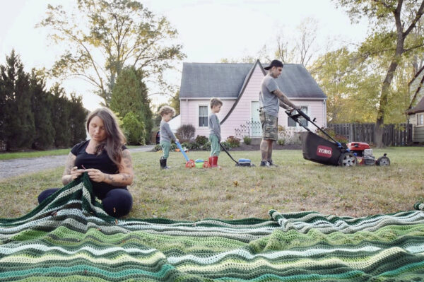 A photograph of artist Madison Hendry knitting a large work made up of green yarn. 